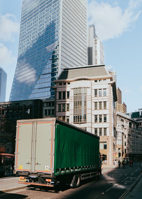 A professional removals team packing and loading household items into a van for home relocation. Inside a residential property, there are several cardboard boxes and plastic-wrapped furniture pieces b